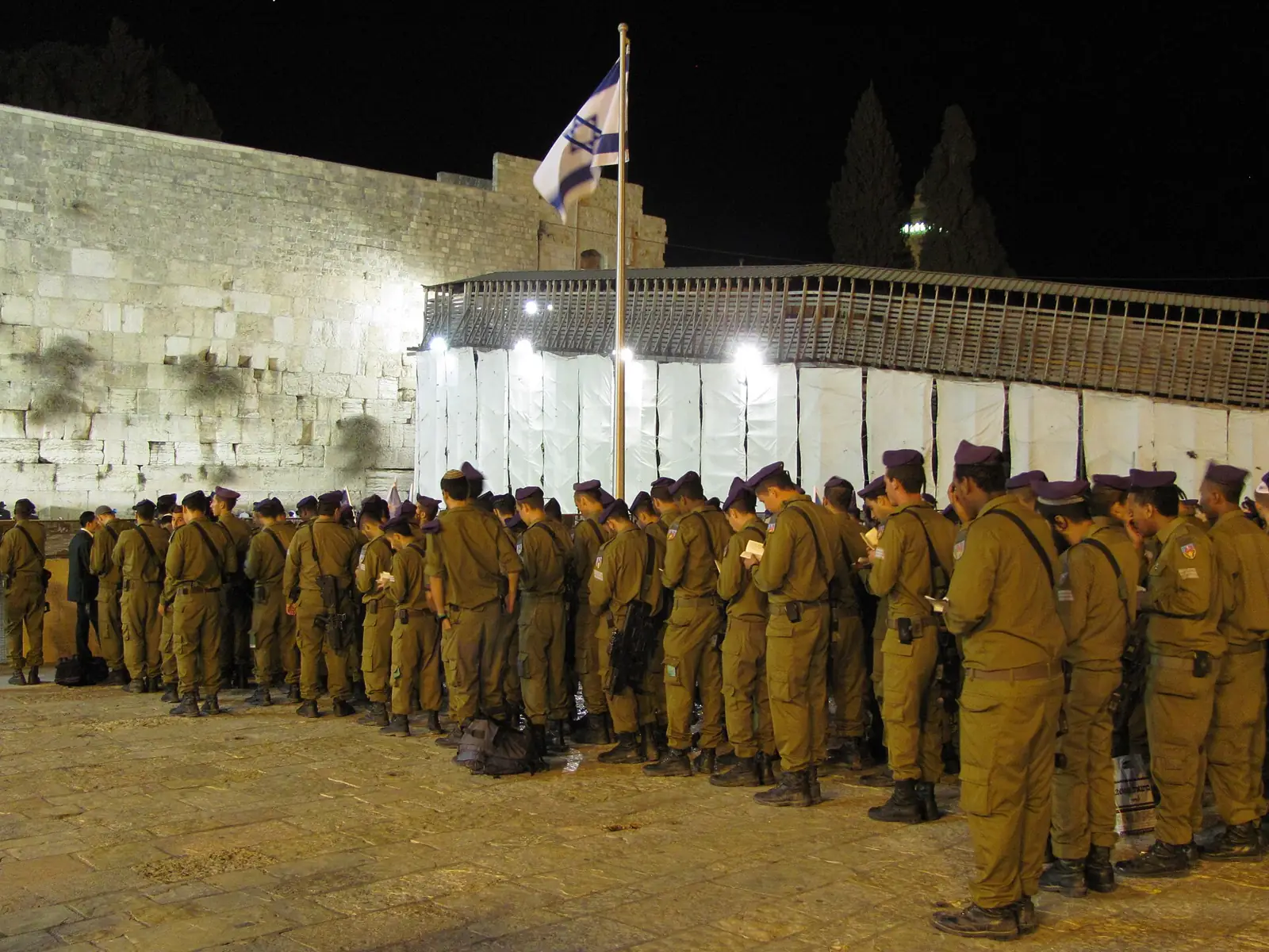 Givati Brigade soldiers standing in formation at the Kotel at night beneath the Israeli flag