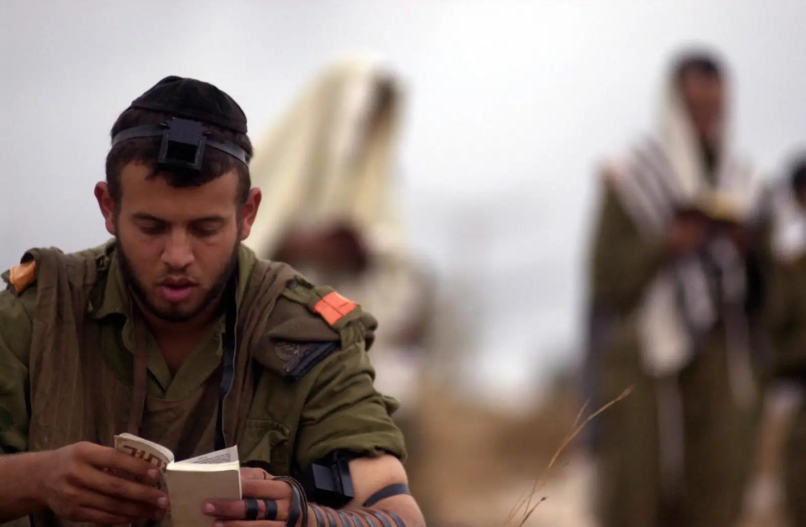 An IDF soldier wearing tefillin davens Shacharis in the field beside soldiers in tallis