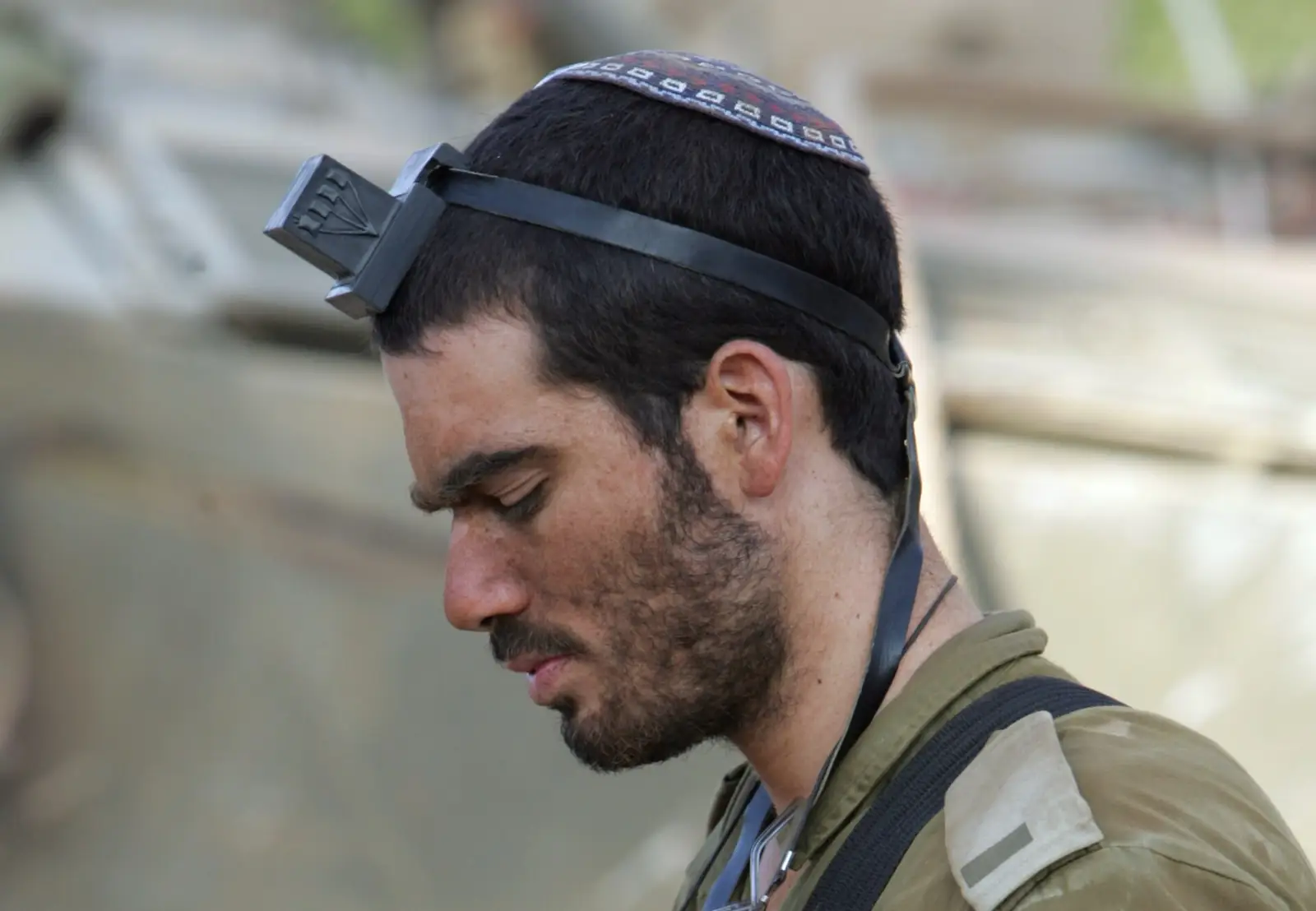 An IDF soldier wearing a kippah and tefillin, head bowed in prayer